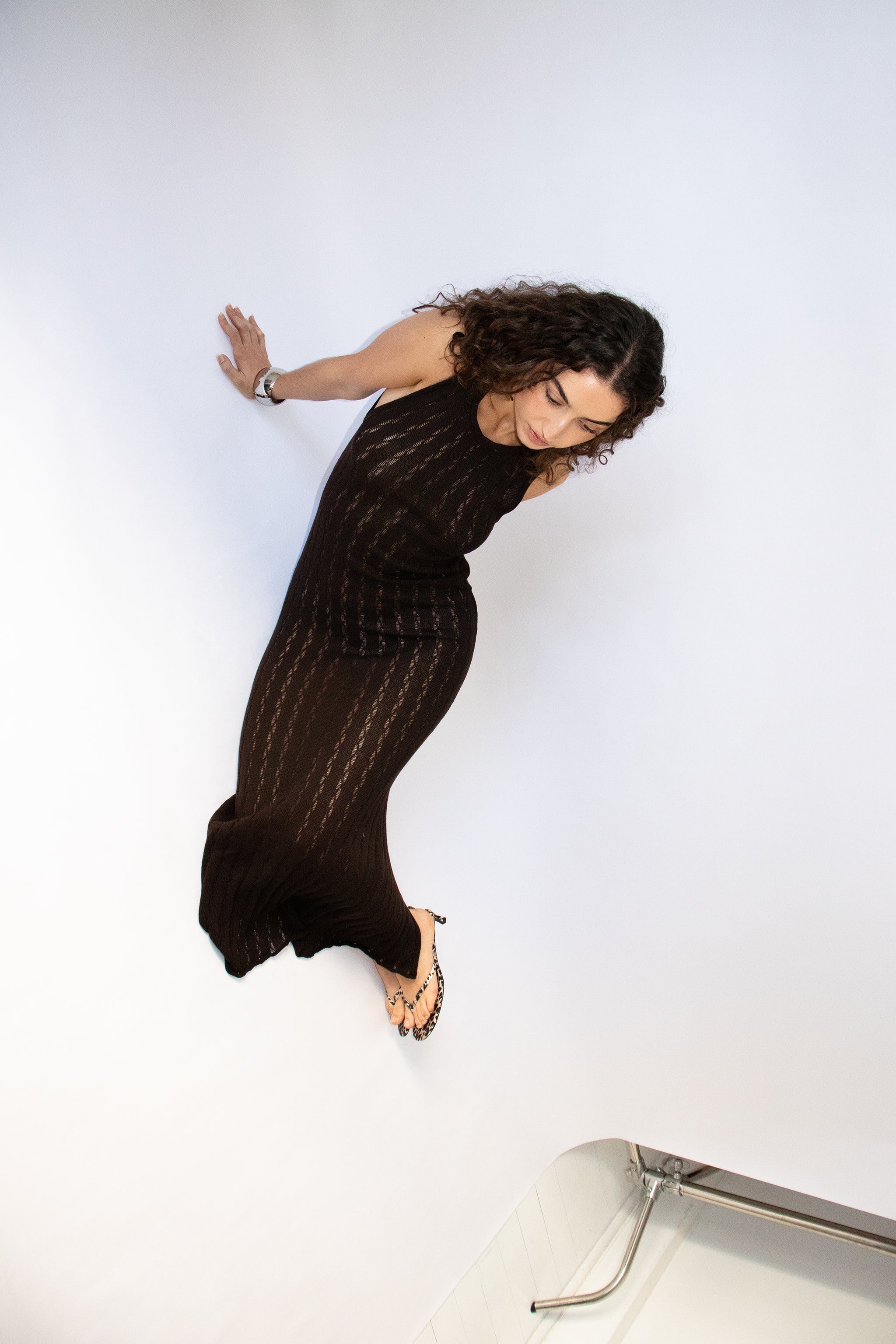 Woman wearing a dark brown sleeveless knit maxi dress with a slit in a studio setting
